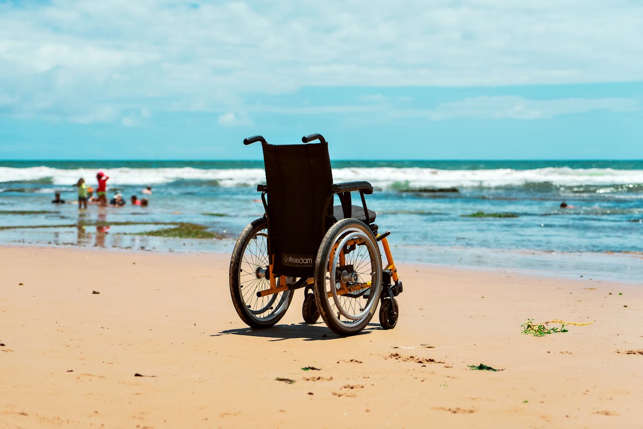 Wheelchair on sandy beach with ocean waves and distant people, highlighting accessibility and leisure.