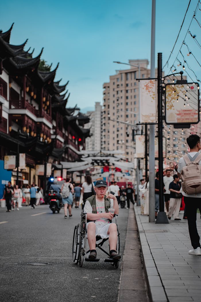 A person in a wheelchair on a busy city street with traditional architecture.