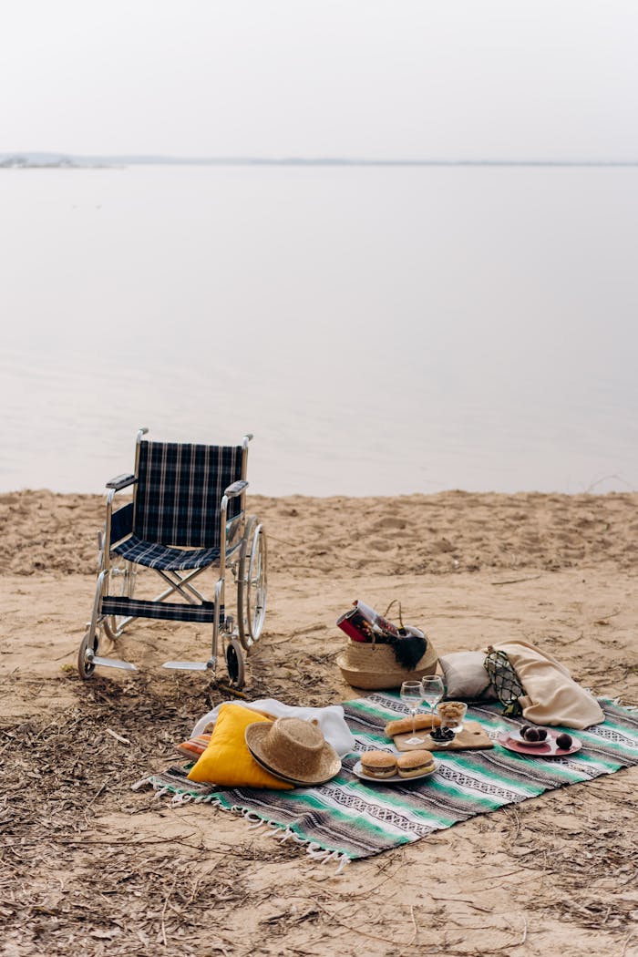 A relaxing beach picnic setup with a wheelchair and essentials by the calm water, evoking accessibility and leisure.